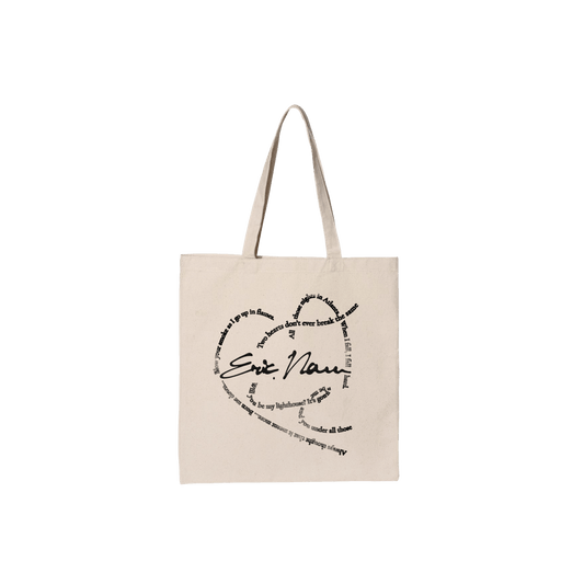 A beige canvas tote bag with two shoulder straps, featuring a black printed graphic on the front that reads 'Eric Nam' in script and block lettering